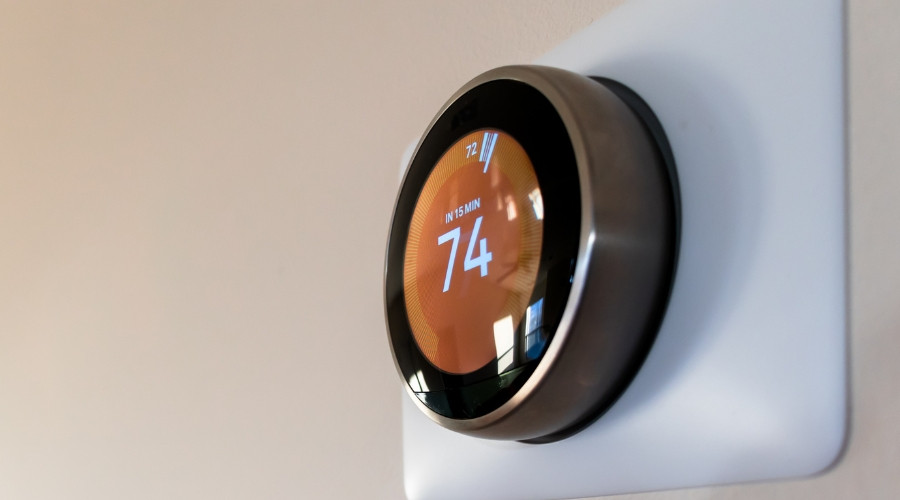 A close-up shot of a round, silver smart thermostat mounted on a white wall.